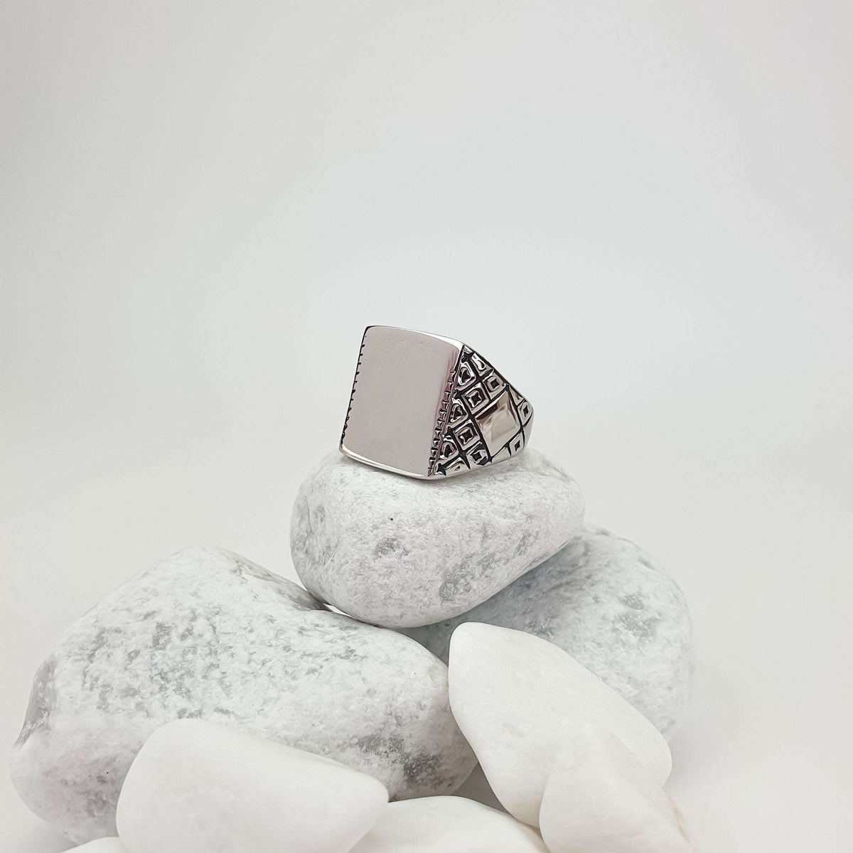 Ring with a shiny engravable plate and relief side patterns on white stones