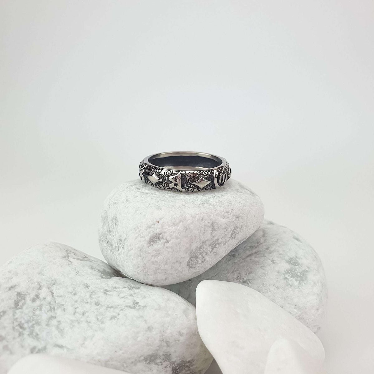 Silver-tone ring with detailed relief symbols on light pebbles