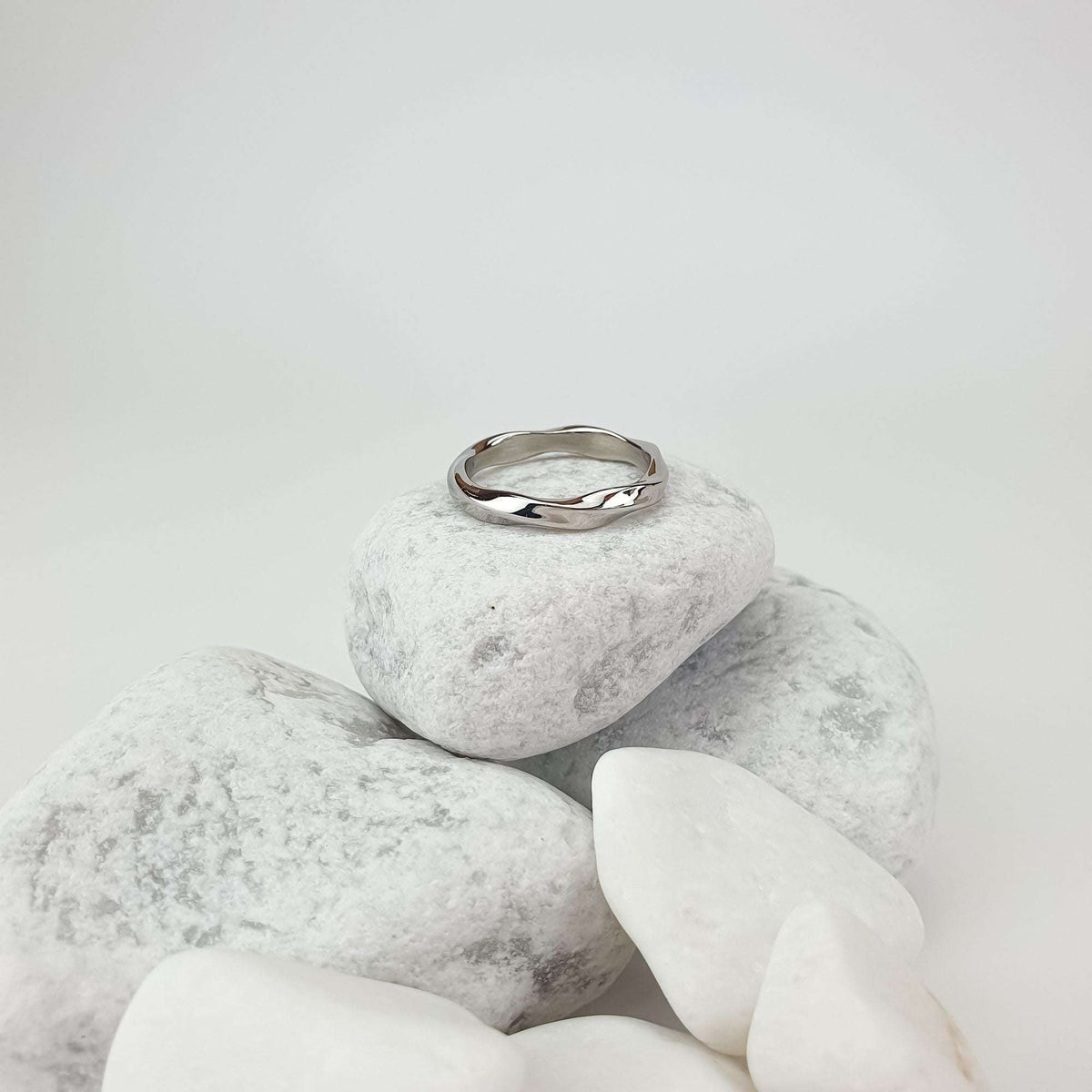 Wavy steel ring on white pebbles showing its shiny polish