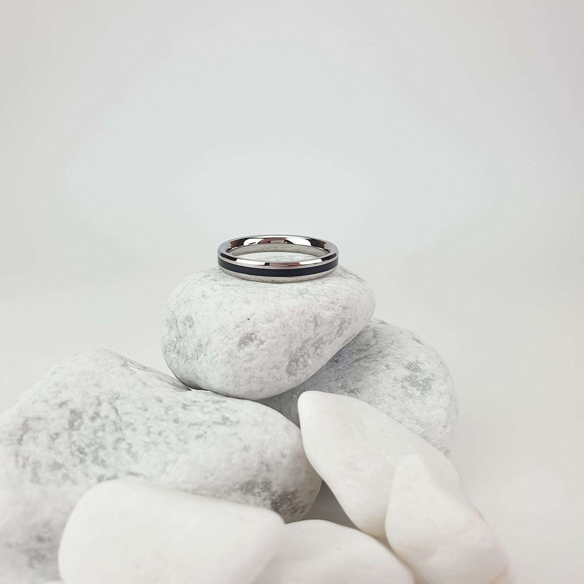 Narrow steel ring with a black stripe, side view on light pebbles