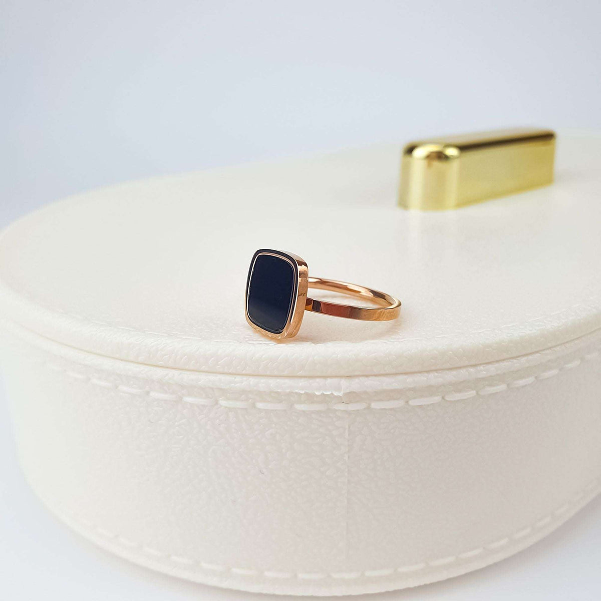 Rose gold-tone ring with black inlay, side view on a white jewellery box