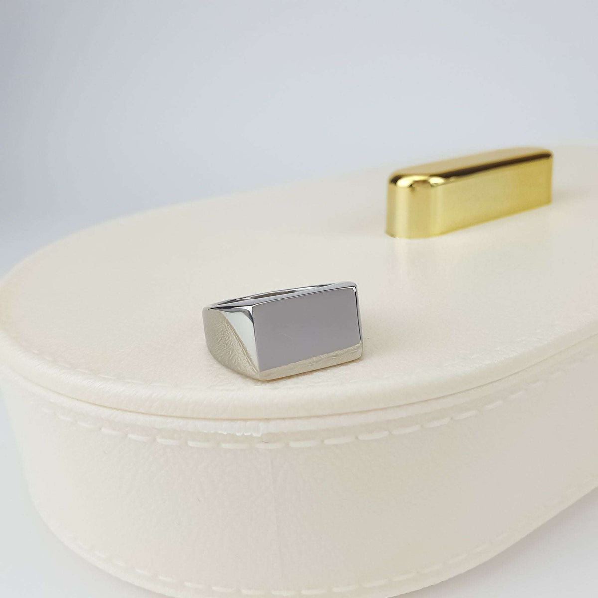 Square steel signet ring on a cream jewellery box, shiny smooth top