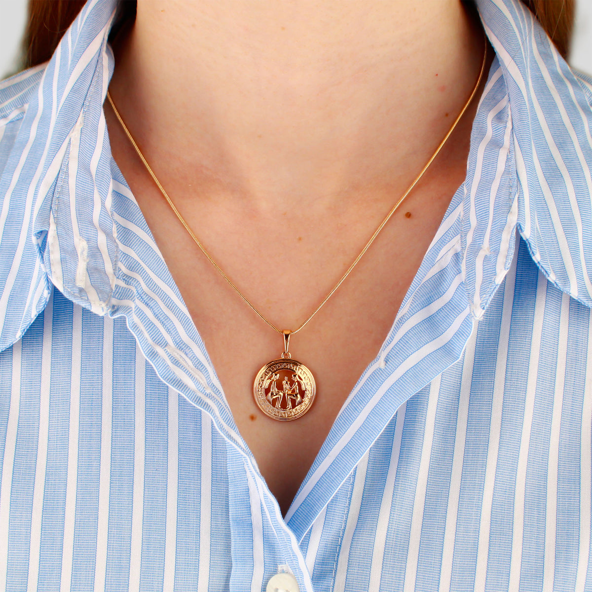 Gold-plated zodiac pendant on a fine chain, worn with a striped shirt