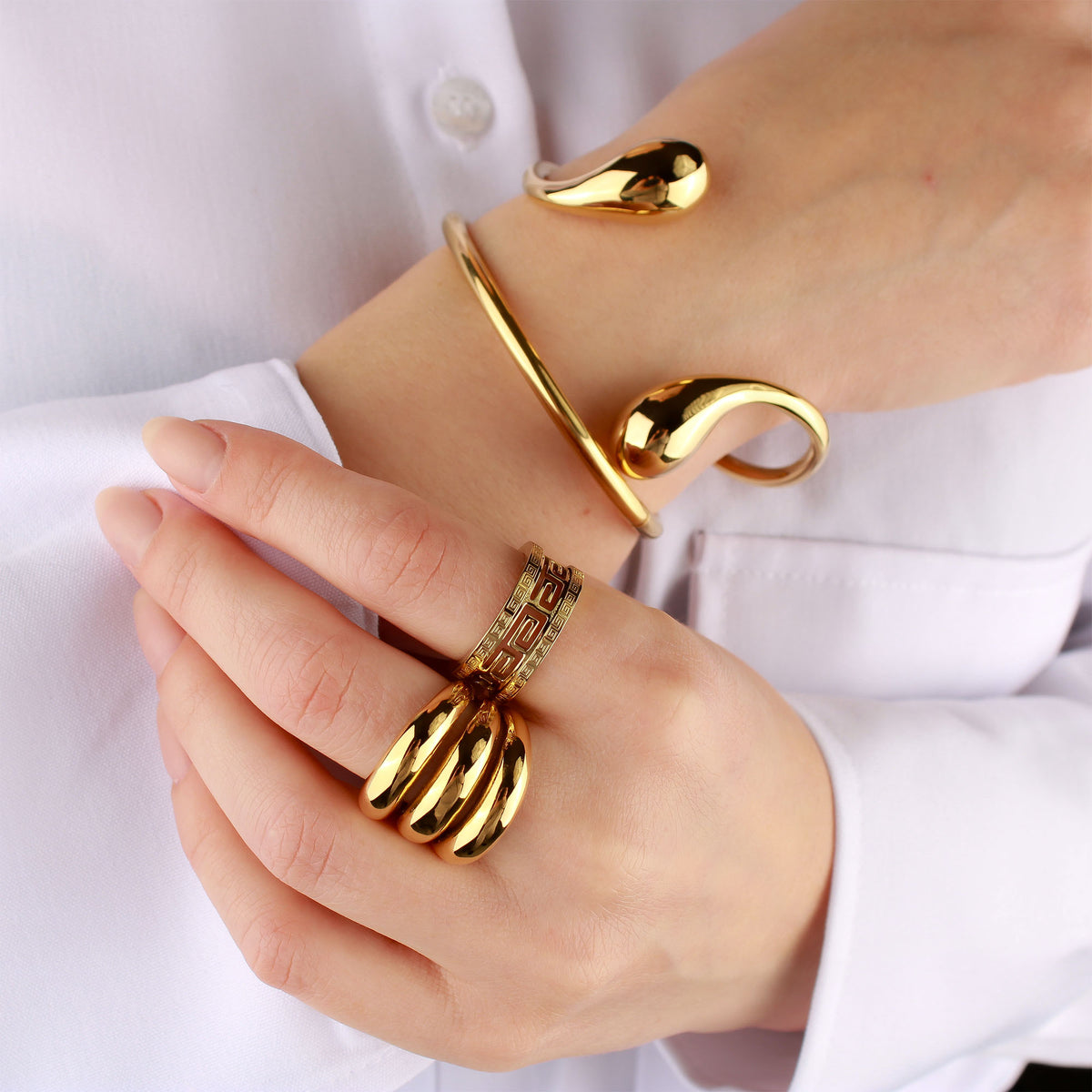 Gold-plated teardrop bangle on a model's wrist with chunky rings and a white shirt