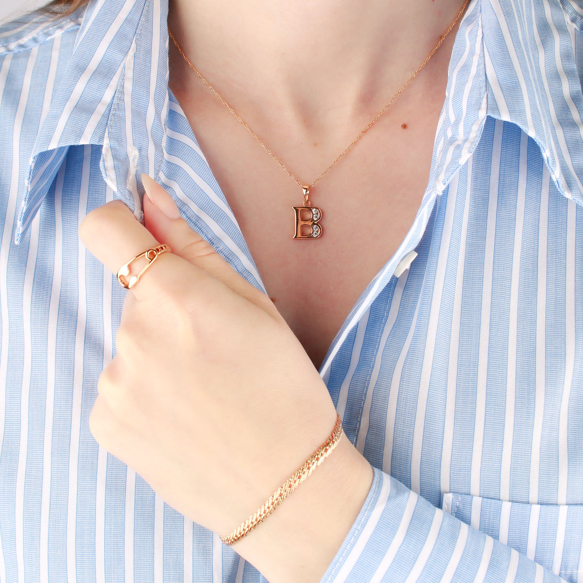 Woman in a blue striped shirt wearing a gold-plated letter B pendant