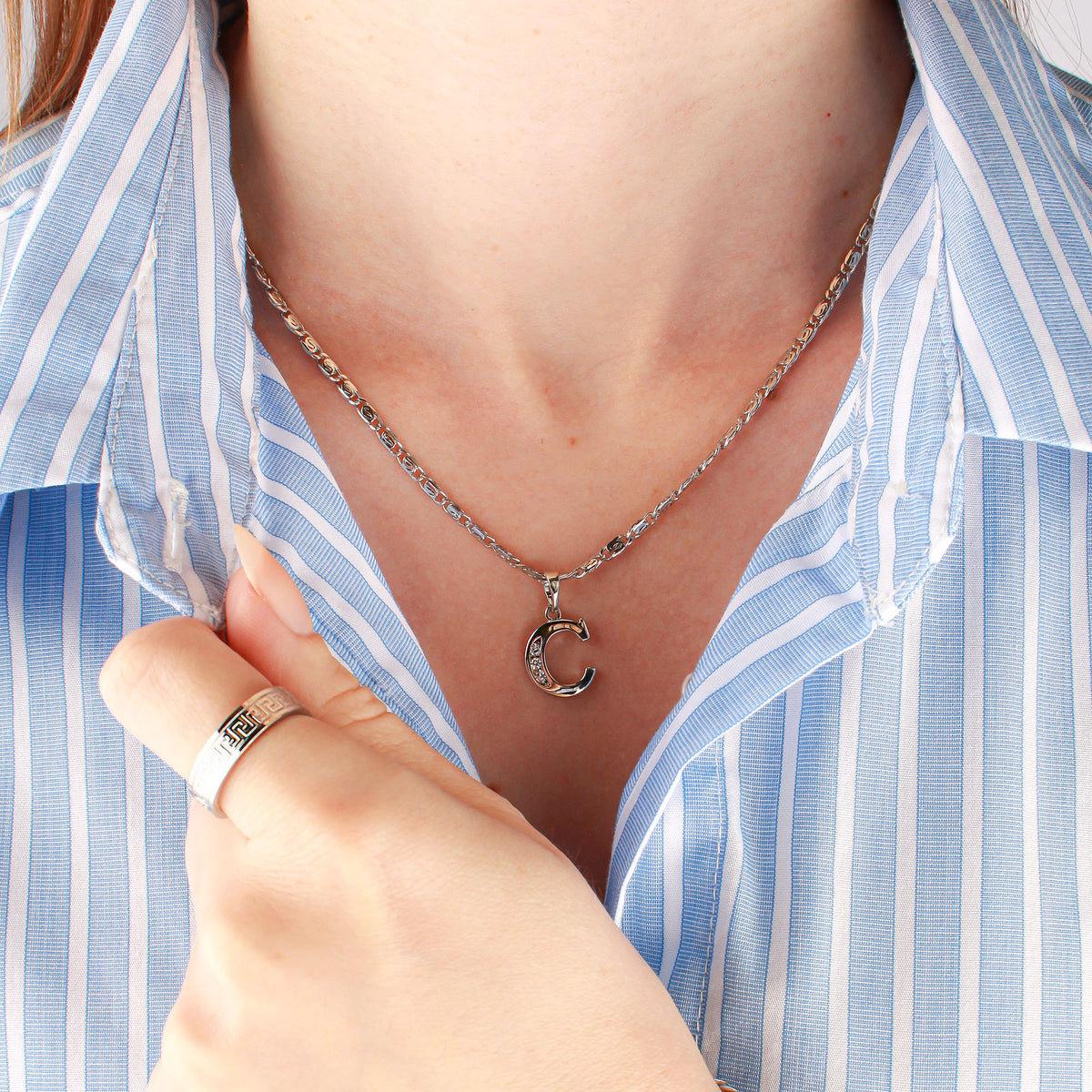 Woman in a blue striped shirt wearing a letter C pendant