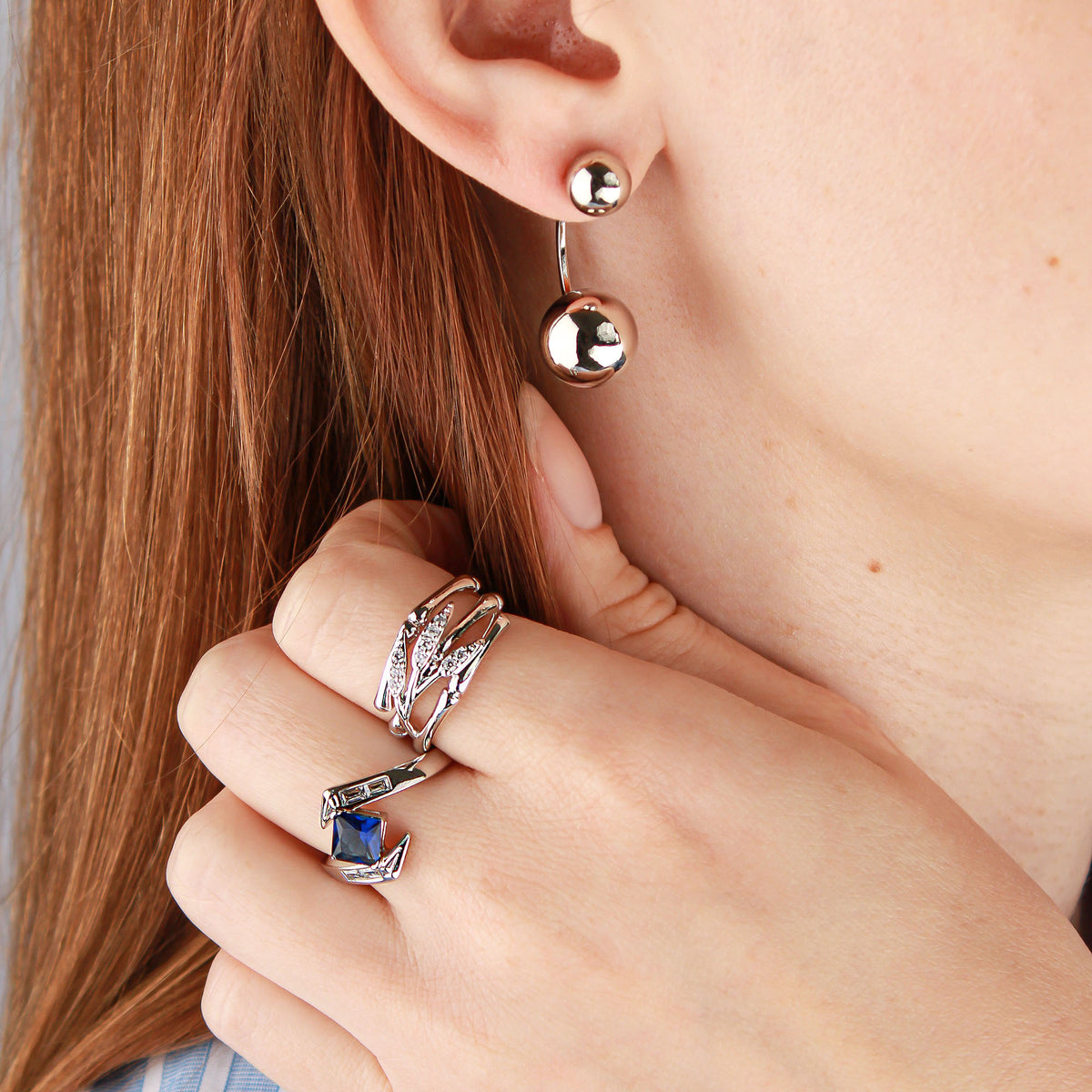 Silver-tone blue stone ring on a model's finger with a ball earring