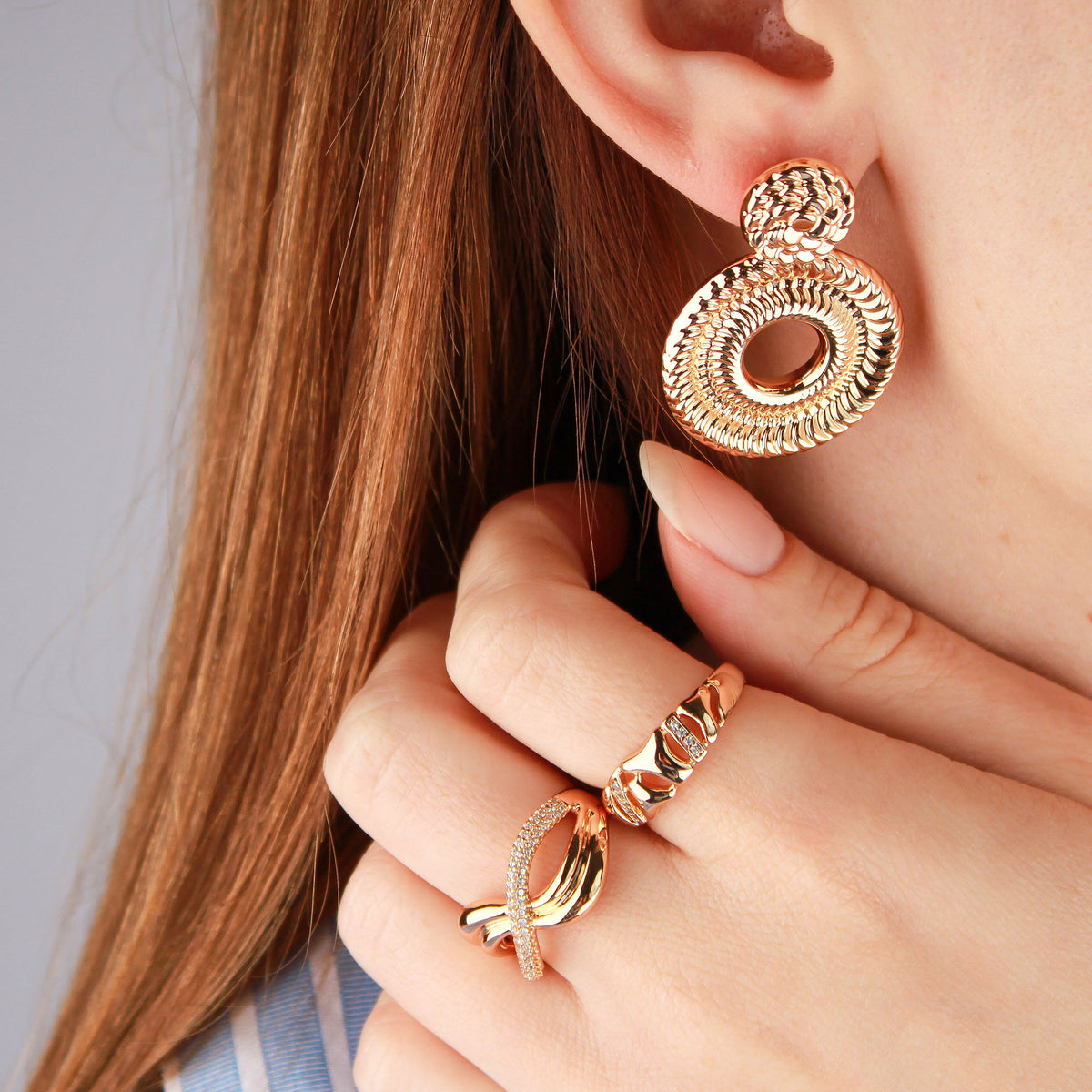 Rose gold-tone cut-out ring on a model's finger beside a chunky round earring